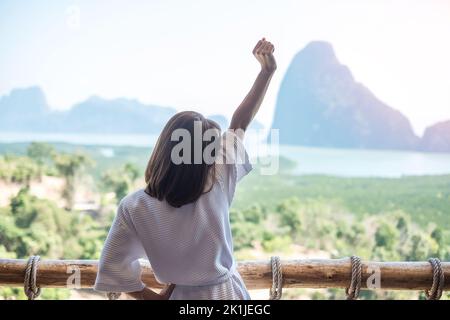 Donna felice in accappatoio stretching dopo il risveglio e godere del punto di vista della baia di Phang Nga, turista rilassante in resort tropicale a Samet Nang She, vicino a Phu Foto Stock