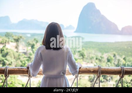 Donna felice in accappatoio stretching dopo il risveglio e godere del punto di vista della baia di Phang Nga, turista rilassante in resort tropicale a Samet Nang She, vicino a Phu Foto Stock