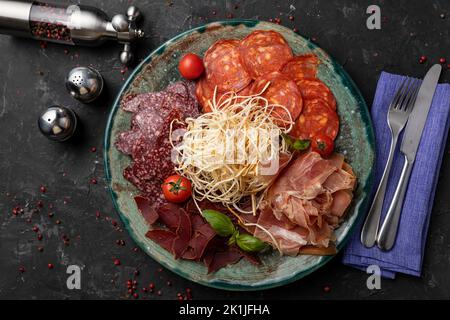 Un primo piano di antipasto di carne con maiale e coltello su fondo nero Foto Stock