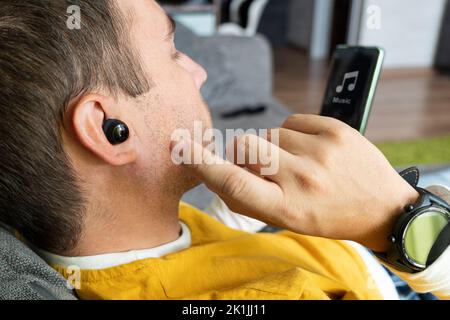 Primo piano dell'auricolare wireless sull'orecchio umano su sfondo scuro. Inserire l'auricolare nell'orecchio. Ascoltare la musica con le cuffie. Foto Stock