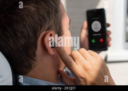 un giovane uomo d'affari riceve una chiamata in arrivo su uno smartphone utilizzando un auricolare wireless Foto Stock