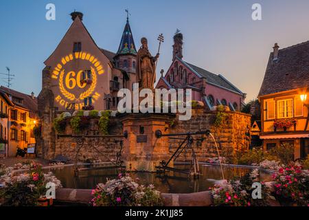 Una serata estiva sulla piazza principale (con la fontana di Saint-Léon) nel villaggio di Eguisheim in Alsazia francese. L'edizione 60th del viticoltore Foto Stock