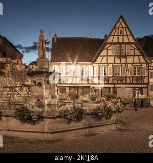 Una serata estiva dopo il tramonto sulla piazza principale (con la fontana di Saint-Léon) nel villaggio di Eguisheim in Alsazia, Francia. Foto Stock