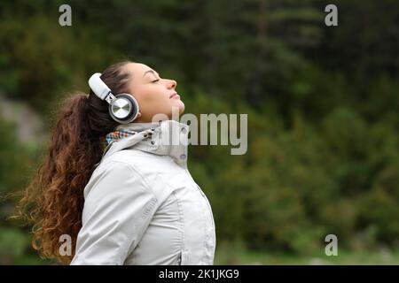 Profilo di un escursionista con cuffie che respirano aria fresca in montagna Foto Stock