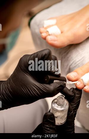 Manicure master pittura unghie su un piede femminile con smalto trasparente unghie in un salone di bellezza, primo piano Foto Stock