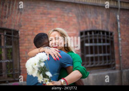 Donna che tiene fiori mentre abbraccia un uomo per strada Foto Stock