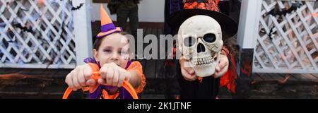 ragazza volto oscuro con cranio spettrale vicino amico in costume clown, banner Foto Stock