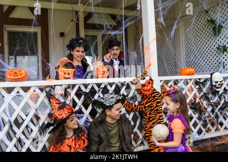 Bambini interrazziali in costumi di Halloween che parlano vicino alla decorazione sulla casa Foto Stock