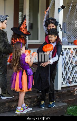 Bambini interrazziali in costumi con zucche mentre festeggia Halloween in cortile Foto Stock