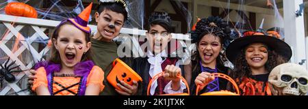 Bambini multietnici che tengono secchi mentre festeggiano Halloween all'aperto, banner Foto Stock