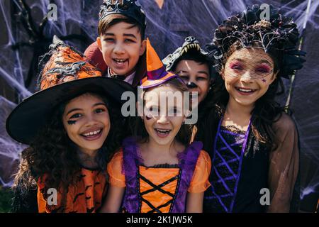 Ragazzi multietnici positivi in costumi di Halloween sorridenti alla fotocamera all'aperto Foto Stock