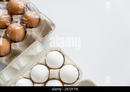 Vista dall'alto di diverse uova in scatole di cartone con cellophane su sfondo bianco Foto Stock