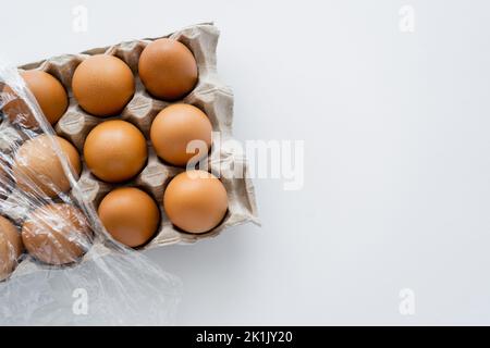Vista dall'alto delle uova marroni nel vassoio di cartone con cellophane su sfondo bianco Foto Stock