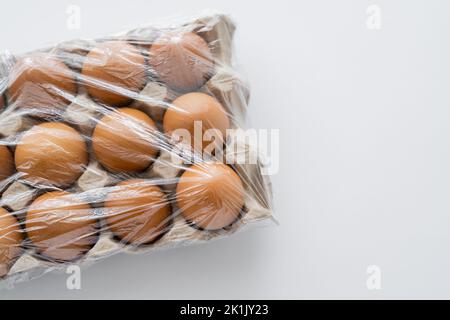 Vista dall'alto di cellofan su uova marroni in vassoio su sfondo bianco con spazio copia Foto Stock