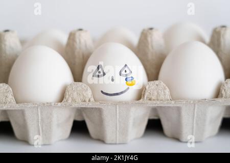 Uovo dipinto con espressione facciale e bandiera ucraina su sfondo bianco Foto Stock
