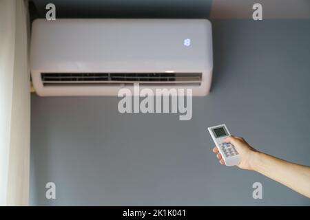 Il proprietario accende il condizionatore d'aria appeso alla parete con telecomando per riscaldare l'appartamento freddo Foto Stock