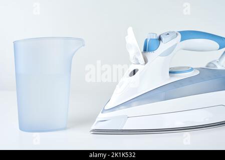 Nuovo ferro da stiro e acqua per il vapore su sfondo bianco, elettrodomestici moderni per la routine quotidiana e le faccende Foto Stock