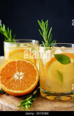 Limonata fatta in casa con arancia e rosmarino, bicchiere di coda di cocco estivo su sfondo scuro, Citrus detox acqua per rinfrescarsi nelle calde giornate estive Foto Stock