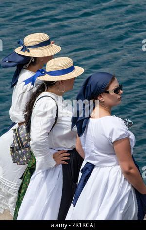 Tre donne in abbigliamento tradizionale: Abiti bianchi, grembiuli blu e teste coperte che si trovano ai margini del molo di Romeria Barquera, Los Abrigos Foto Stock
