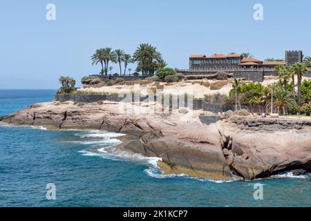 Vista sulla costa rocciosa, le onde dell'oceano e l'edificio sopraelevato noto come Casa del Duque circondato da giardini tropicali, del Duque, Costa Adeje Foto Stock