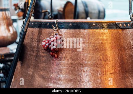 Mazzo di uve appeso al vaso di VIN brulé in una stalla in un mercatino di Natale. Primo piano di VIN brulé in tradizionale calderone di rame. Stagionale c Foto Stock