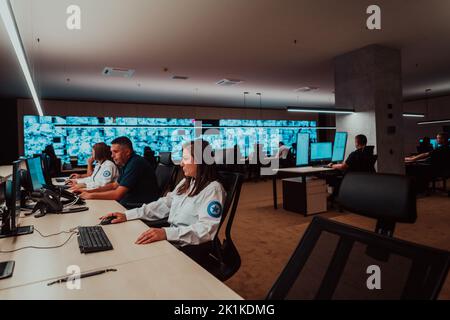 Gruppo di operatori del data center di sicurezza che lavorano in una sala di monitoraggio TVCC alla ricerca di più monitor funzionari che monitorano più schermi per Foto Stock