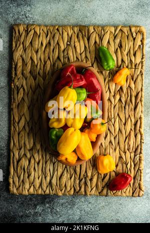 Vista dall'alto di una ciotola di legno riempita con peperoncini rossi, verdi e gialli assortiti su un tappetino da tavolo Foto Stock