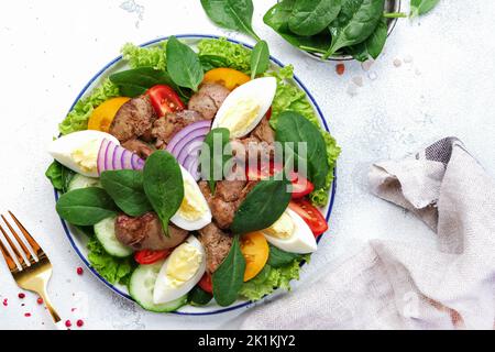 Insalata di perigord con fegato di pollo, pomodori, cetrioli, uova, lattuga e spinaci. Sfondo bianco tavolo da cucina, vista dall'alto Foto Stock