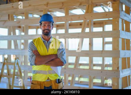 Lavoratore di costruzione in abiti protettivi posa in eco cantiere di legno telaio casa. Foto Stock