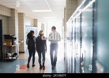 Insegnante di scuola superiore e studenti che camminano in corridoio soleggiato