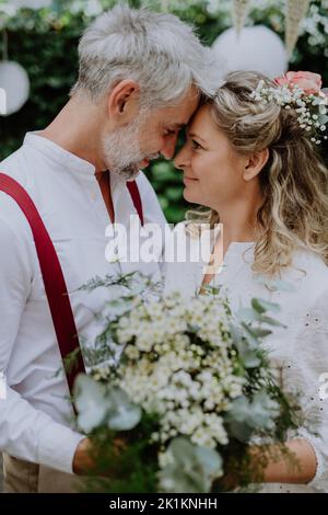 Sposa matura e sposo avere un momento romantico al ricevimento di nozze fuori nel cortile. Foto Stock