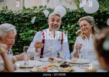 Sposa matura e sposi con gli ospiti al ricevimento di nozze all'esterno nel cortile. Foto Stock