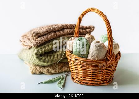 Fili di filo verde e marrone in un cesto per maglieria di abiti caldi con aghi per maglieria e prodotti finiti in filo, hobby per maglieria Foto Stock