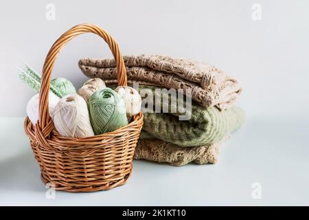 Fili di filo verde e marrone in un cesto per maglieria di abiti caldi con aghi per maglieria e prodotti finiti in filo, hobby per maglieria Foto Stock