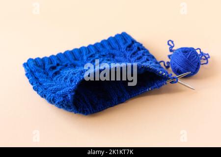 Maglieria di abiti caldi blu con aghi da maglieria e palle di filo blu su sfondo arancione Foto Stock
