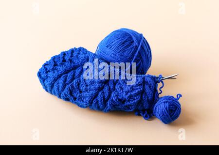 Maglieria di abiti caldi blu con aghi da maglieria e palle di filo blu su sfondo arancione Foto Stock