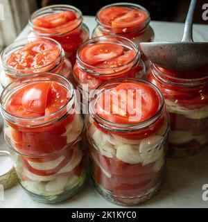 Inscatolamento di pomodori freschi con cipolle per l'inverno in marmellata di gelatina. Un colpo di foglie di basilico sopra una fetta di pomodoro matura rossa e anelli di cipolla che vengono messi io Foto Stock