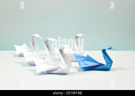 Un cigno blu conduce un gregge di cigni bianchi. La carta si gonfia su sfondo blu. Origami. Concetto di leadership. Foto Stock