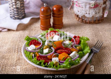 Insalata calda con zucca, formaggio feta, pomodori secchi, olive, rucola e cipolla rossa. Primo piano. Foto Stock