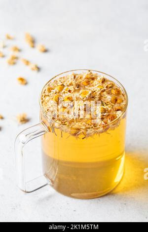 Tè di camomilla con fiori in una tazza di vetro. Bevanda salutare a base di erbe, antisettico naturale e aiuto alla digestione. Foto Stock