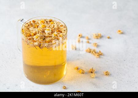 Tè di camomilla con fiori in una tazza di vetro. Bevanda salutare a base di erbe, antisettico naturale e aiuto alla digestione. Foto Stock