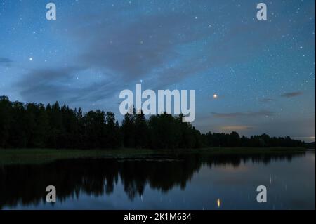 Paesaggio notturno sotto il cielo stellato. Costellazioni Gemini e Orion che si innalzano sopra l'orizzonte, stelle che si riflettono dalla superficie dell'acqua calma. Foto Stock