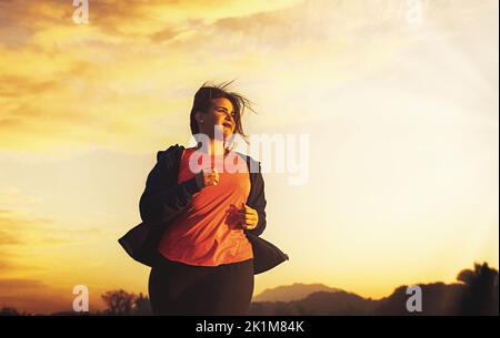 Una bella giovane donna più dimensione jogging nella natura al tramonto o all'alba determina il peso sciolto - persone, sport, corpo positivo e perdita di peso l Foto Stock