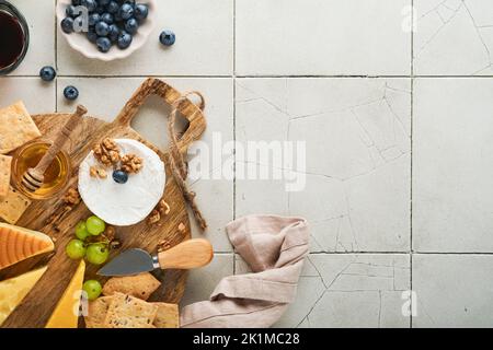 Assortimento di formaggi, miele, cracker, mirtilli, uva con vino rosso e bianco in bicchieri antipasto server su tavola di marmo bianco su fondo grigio Foto Stock