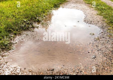 Puddle su strada sterrata dopo la pioggia. Strada fangosa in campagna. Strada bagnata. Strada del coltivatore tra i campi nella Repubblica Ceca. Foto Stock