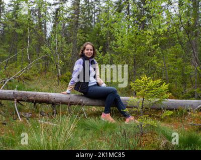 donna seduta su un albero caduto in una foresta verde Foto Stock