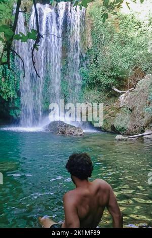 Vista posteriore dell'uomo che guarda una cascata nelle montagne. Foto Stock