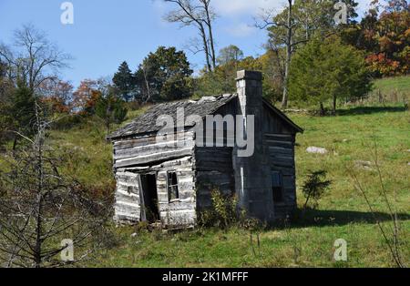 Vecchia capanna di legno con tetto in ciottoli di legno, si trova abbandonata su una collina nei Monti Appalachi. La porta rimane aperta. Foto Stock