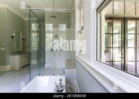 Bagno verde salvia con finiture bianche dover, vasca indipendente, doccia chiusa con vetro con mattoni a spina di pesce dipinti in bianco, piano di granito Foto Stock