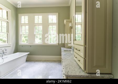 Bagno verde salvia con finiture bianche dover, vasca indipendente, doccia chiusa con vetro con mattoni a spina di pesce dipinti in bianco, piano di granito Foto Stock